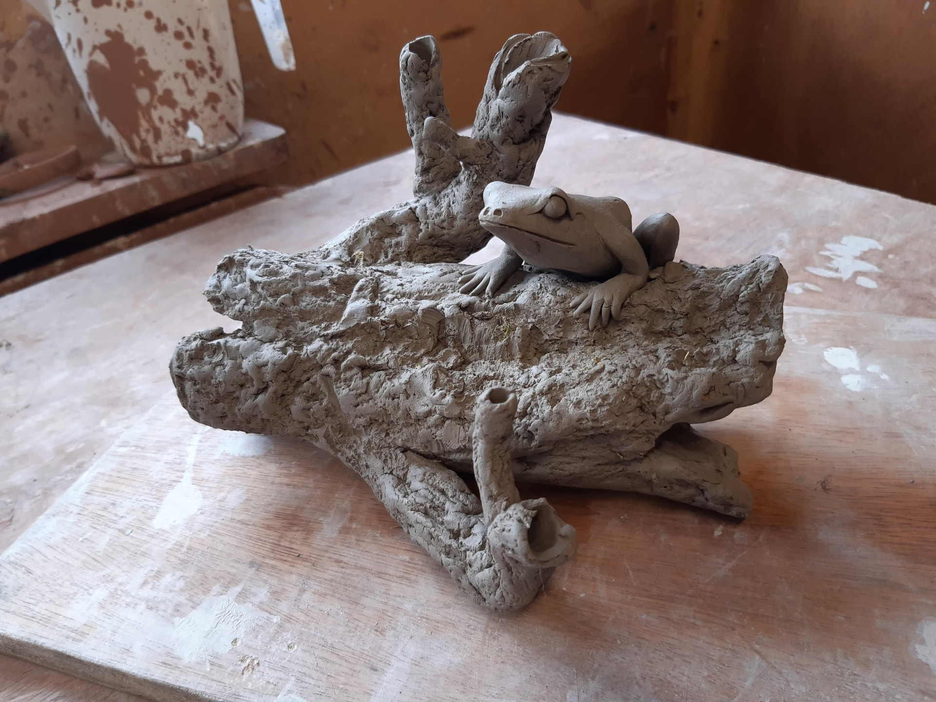 A modelled clay frog resting on a hollowed log.