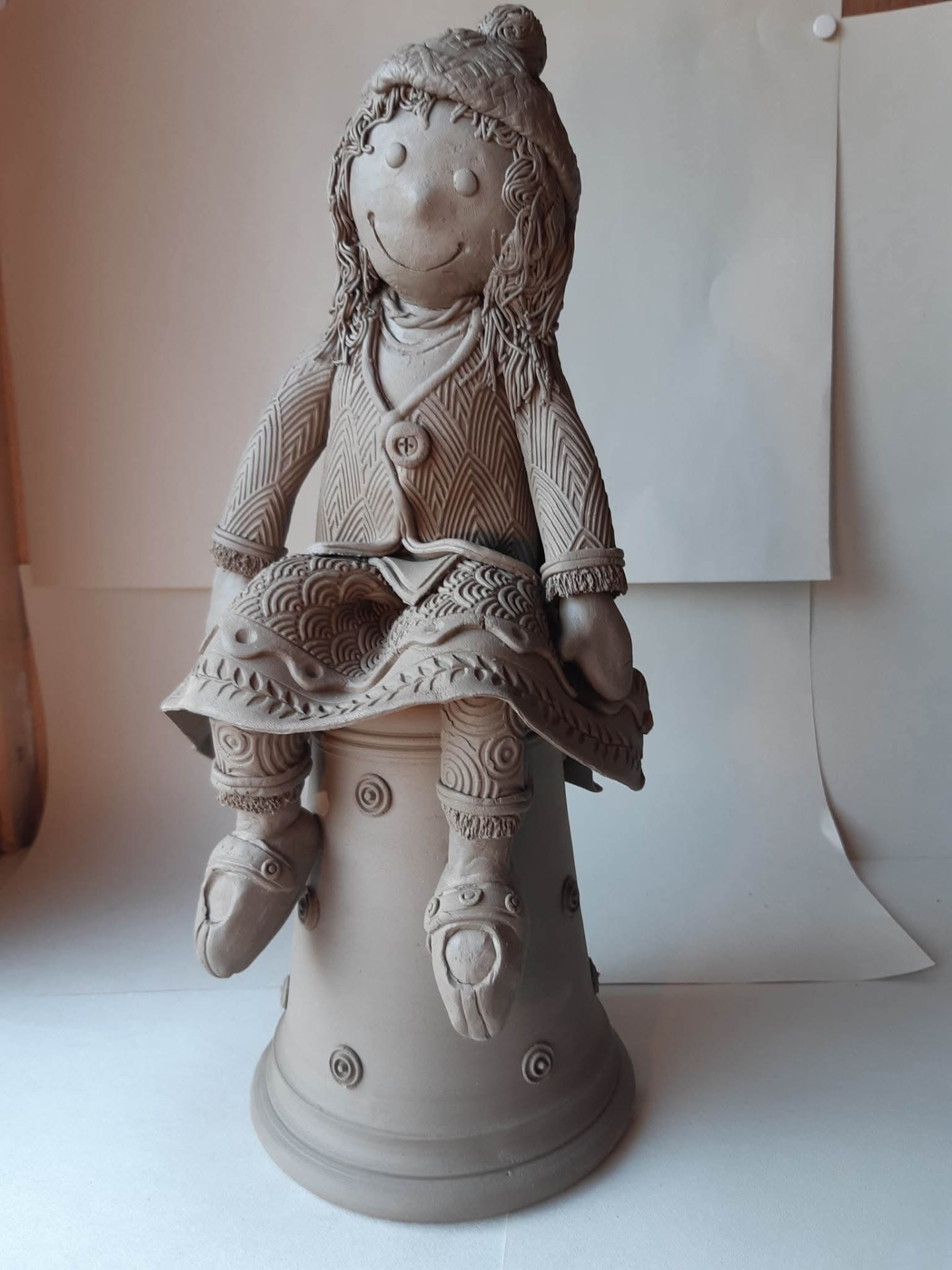 A clay girl figure wearing a dress patterned with carved lines and circles.
